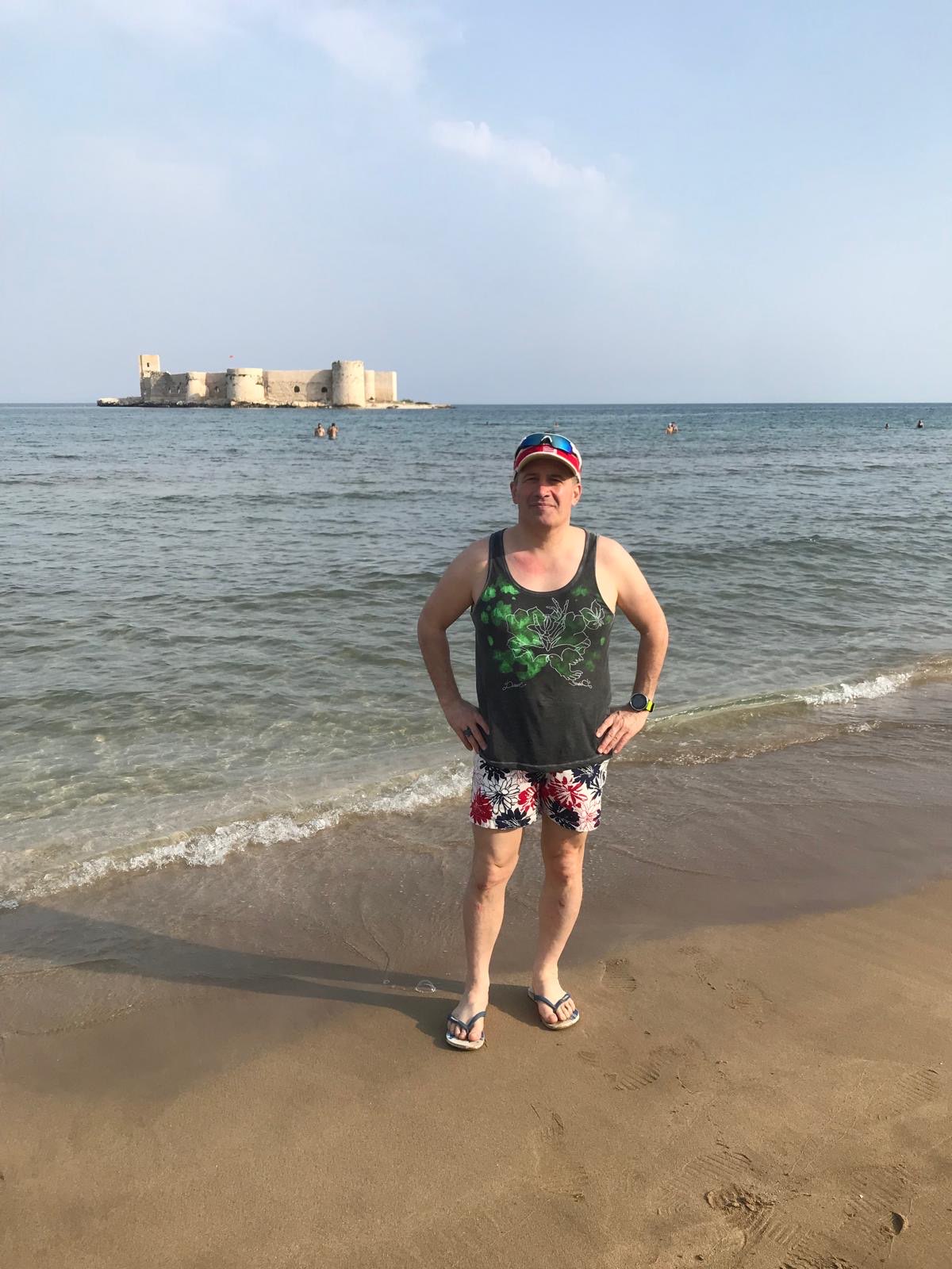 Erden Giritli on a beach with a castle view, reflecting his healthy lifestyle coach identity